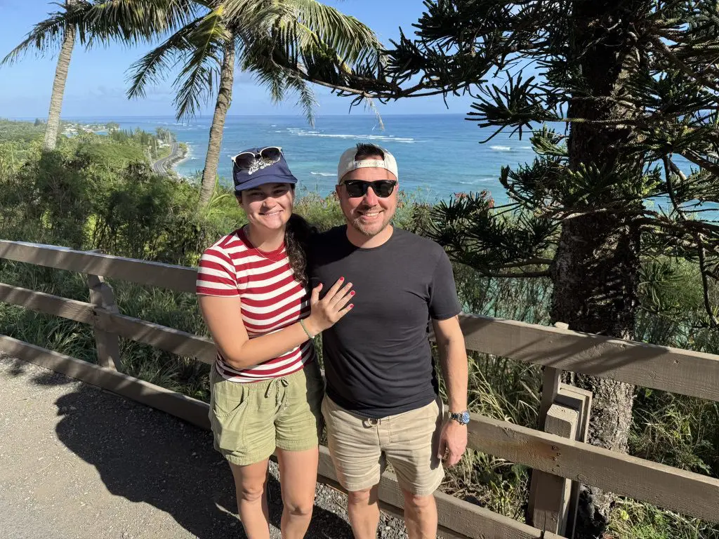 Couple smiling by ocean, palm trees behind.